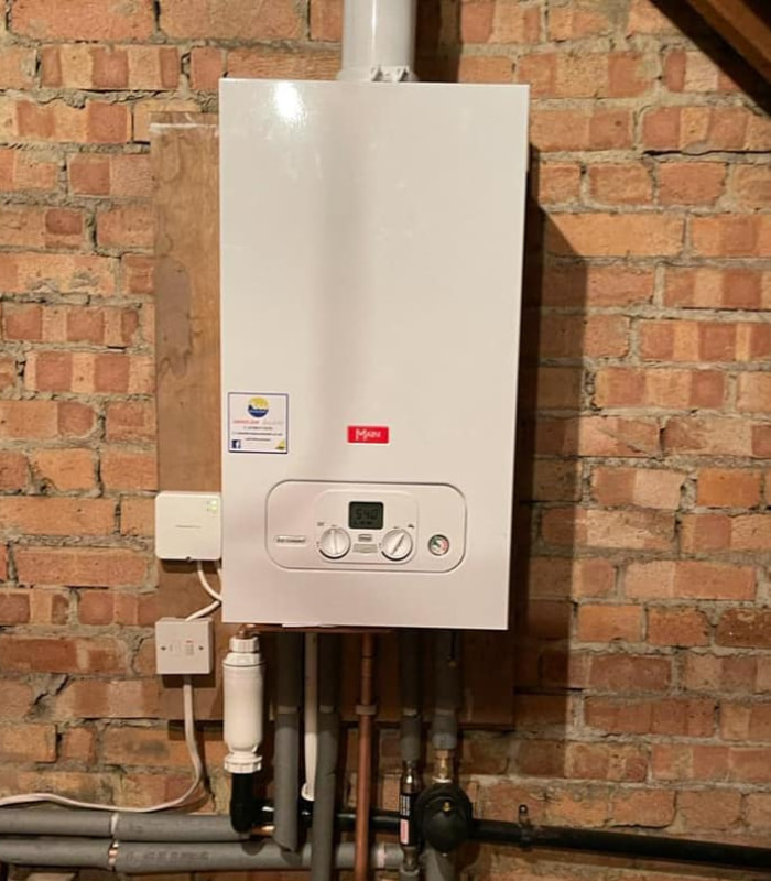 A recently serviced boiler installed on an unpainted brick wall. The RTW Plumb Safe service sticker can be seen to the left of the manufacturer's logo