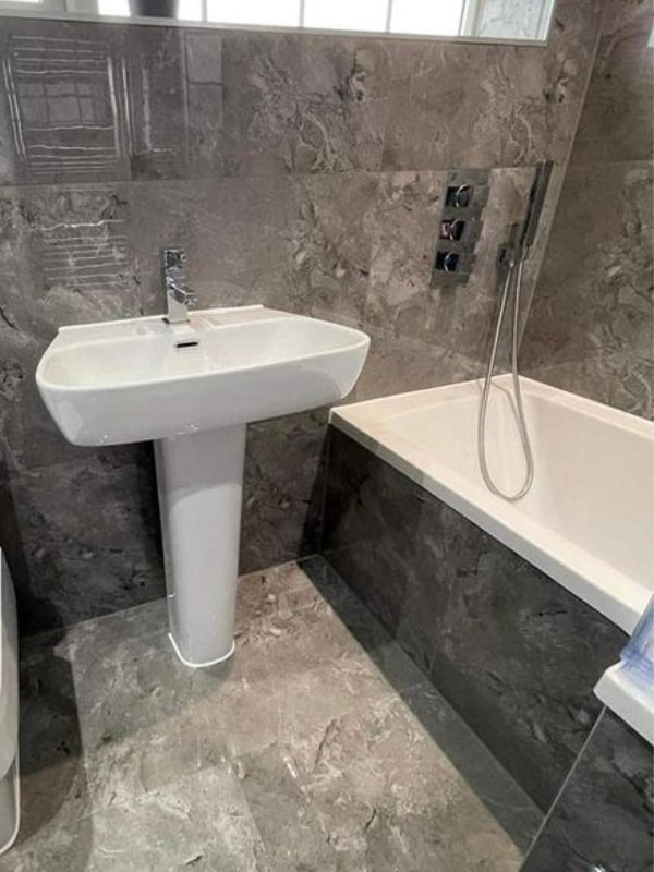 Close-up of the sink and the bath directly next to it. The side of the bath is lined with dark marble tiles