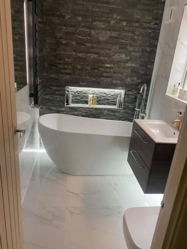 View through the doorway showing the dark walls and curved bathtub illuminated by the lighting installed under the floating sink unit